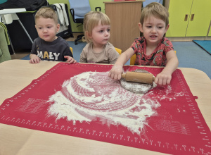 chłopiec wałkuje ciasto, inne dzieci patrzą