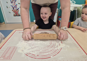 chłopiec wałkuje ciasto i śmieje się, opiekunka mu pomaga