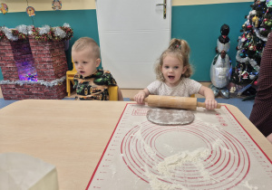 dziewczynka wałkuje ciasto, obok siedzi chłopiec