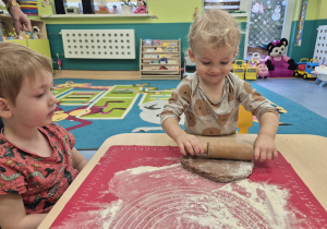 chłopiec wałkuje ciasto, obok siedzi chłopiec i patrzy