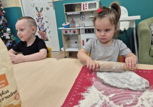dziewczynka wałkuje ciasto, obok siedzi chłopiec