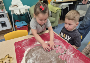 dziewczynka wykrawa foremką ciasto a chłopiec patrzy