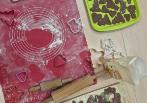 na stoliku leży stolnica wałek i wykrojone pierniczki ułożone na tackach