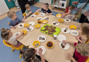 dzieci siedzą przy stole dekorują pierniczki, a opiekunki pomagają