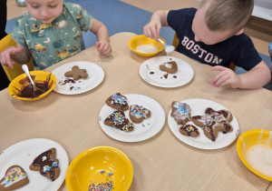 chłopcy siedzą przy stole, jeden polewa piernika lukrem, a drugi się zastanawia
