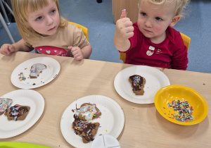 chłopiec pokazuje palec oblepiony kolorową posypką, dziewczynka na niego patrzy