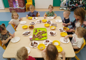 dzieci siedząprzy stole i dekorują pierniczki , opiekunki im pomagają