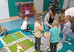 dzieci i opiekunki zbieraja kulki papierowe na dywanie