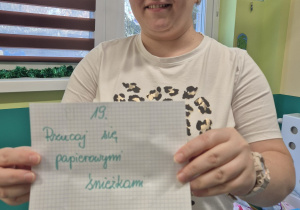 opiekunka trzyma kartke z kalendarza adwentowego z napisem:rzucaj się śnieżkami z papieru