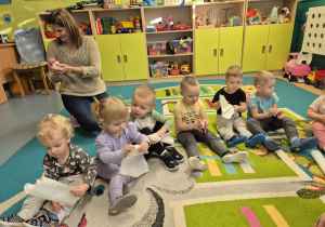 dzieci i opiekunka siedzą na dywanie i gniotą papier