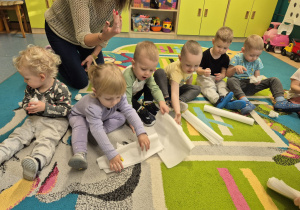 dzieci siedzą na dywanie i gniota piapier, robią kulki