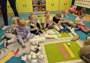 dzieci siedza na dywanie, a przed nimi dużo kulek papierowych