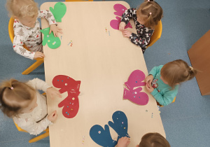 dzieci siedza przy stoliku, przed nimi leżą rękawiczki, które ozdabiają