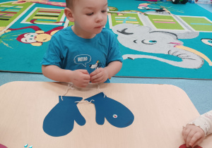 chłopiec siedzi przy stoliku , patrzy, przed nim leżą rękawiczki