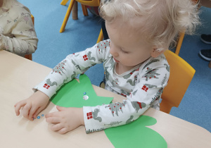 chłopiec siedzi przy stoliku , przykleja perełki