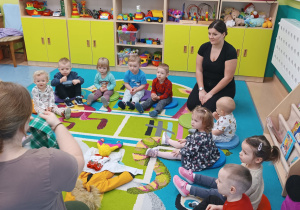 dzieci wraz z opiekunkami siedzą na dywanie , wybierają ubrania na zimę