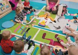 dzieci i opiekunki siedza na dywanie, wybierają ubrania i układaja je na dywanie