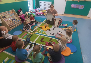 dzieci siedzą na dywanie , opiekunka pokazuje ubrania