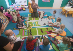 dzieci i opiekunki siedza na dywanie, opiekunka pokazuje ubrania