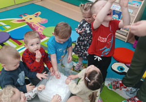 dzieci dotykają śniegu w pojemniku, chłopiec się uśmiecha