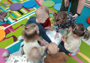 dzieci dotykają śniegu w pojemniku, opiekunka pomaga dziecku