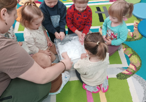 dzieci dotykają śniegu w pojemniku, opiekunka pomaga maluszkowi