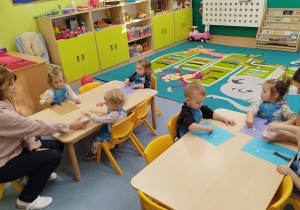 dzieci siedzą przy stolikach wykonują pracę plastyczną, opiekunki im pomagają