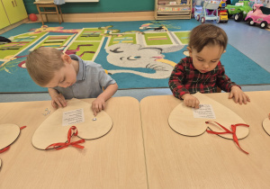 chłopcy siedzą przy stoliku i naklejają serduszka na drewnianym sercu