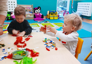 chłopcy siedzą przy stoliku., przyklejają piórka