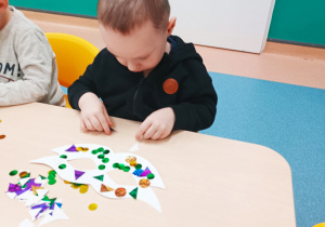 chłopiec siedzi przy stoliku, wybiera ozdoby