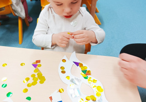 chłopiec trzyma w palcach błyszczące ozdoby do maski