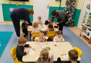 dzieci siedzą przy stolikach ozdabiają maski, opiekunki pomagają
