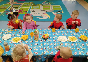 dzieci siedzą przy stoliku,jedzą i piją