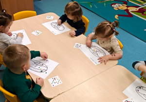dzieci przy stoliku wyklejają wydrukowane pączki