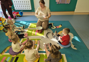dzieci wraz z opiekunką siedza na dywanie