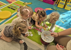 dzieci wrzucaja wybrane obrazki do garnka, a opiekunka miesza łyżką