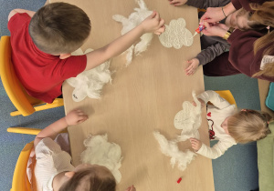 dzieci siedzą przy stoliku i przyklejają watę