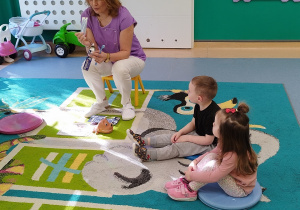 opiekunka pokazuje dzieciom siedzącym na dywanie szczoteczkę i pastę do zębów