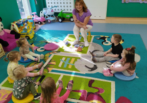 opiekunka pokazuje dzieciom siedzącym na dywanie nić dentystyczną