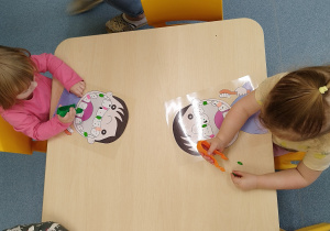 dzieci siedzą przy stoliku, i szczypcami zbierają kulki plasteliny