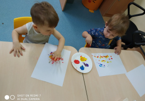 chłopiec macza palec w farbie i maluje na kartce