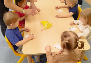 dzieci przyklejają elementy do wyciętej z kartonu rączki, opiekunki pomagają