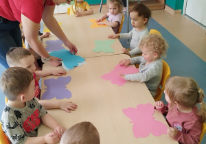dzieci siedzą przy stoliku, opiekunka rozdaje motyle