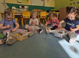 dzieci siedzą, przed nimi stoją pudełka , w którym pracują rączkami