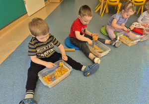 dzieci siedzą na podłodze i bawią się tym co mają w pudełkach przed sobą