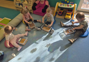 dzieci siedzą i bawią się tym, co mają przed sobą w pudełku