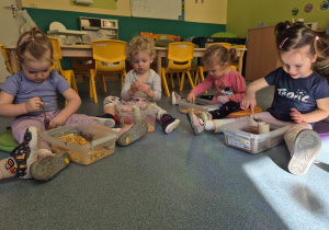 dzieci bawią się tym co mają w pudełku rączkami , kubkami, i łyżeczką