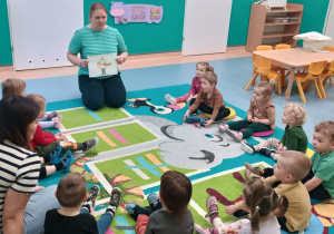 opiekunka czyta zagadkę dzieciom siedzącym na dywanie