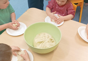 opiekunka rozdaje dzieciom kulkę ciasta