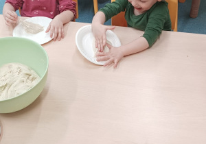 dzieci ugniatają kulki z ciasta na talerzyku